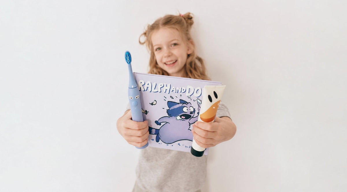 Mädchen zeigt Schallzahnbürste, Kinderzahnpasta und Zahnputzbuch