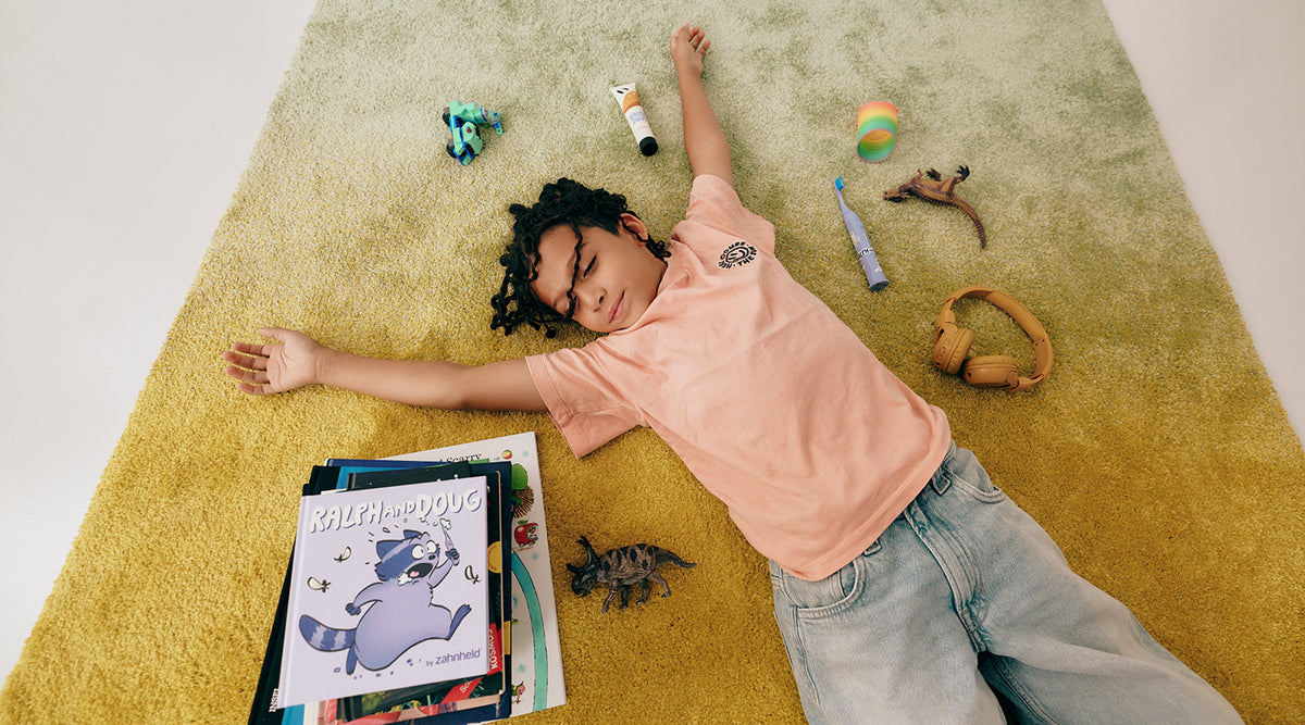 Kind liegt auf dem Teppich mit Spielzeug, Zahnbürste und Bücher